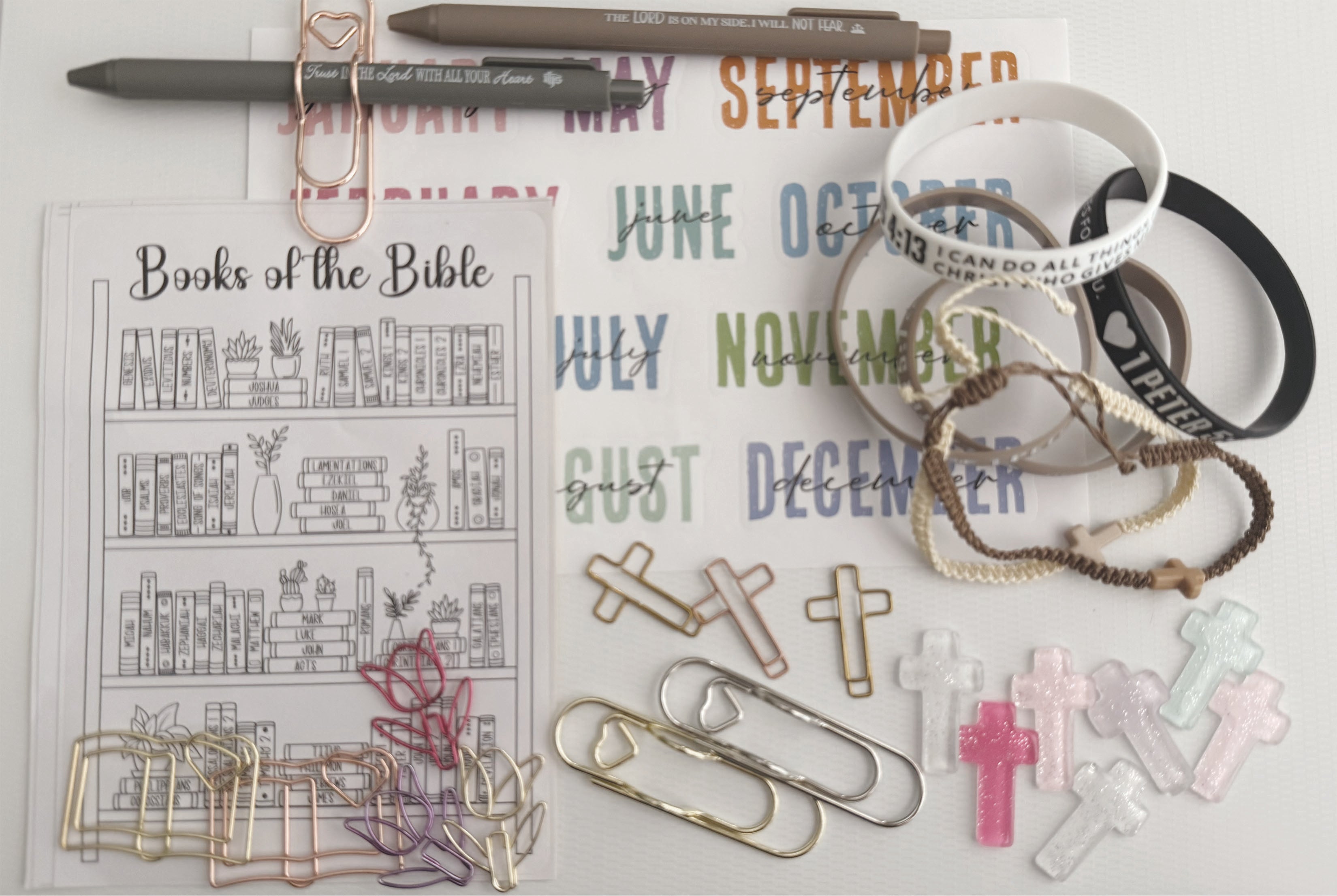 Faith journaling tools with Books of the Bible tracker, month stickers, cross clips, pens, and paper clips